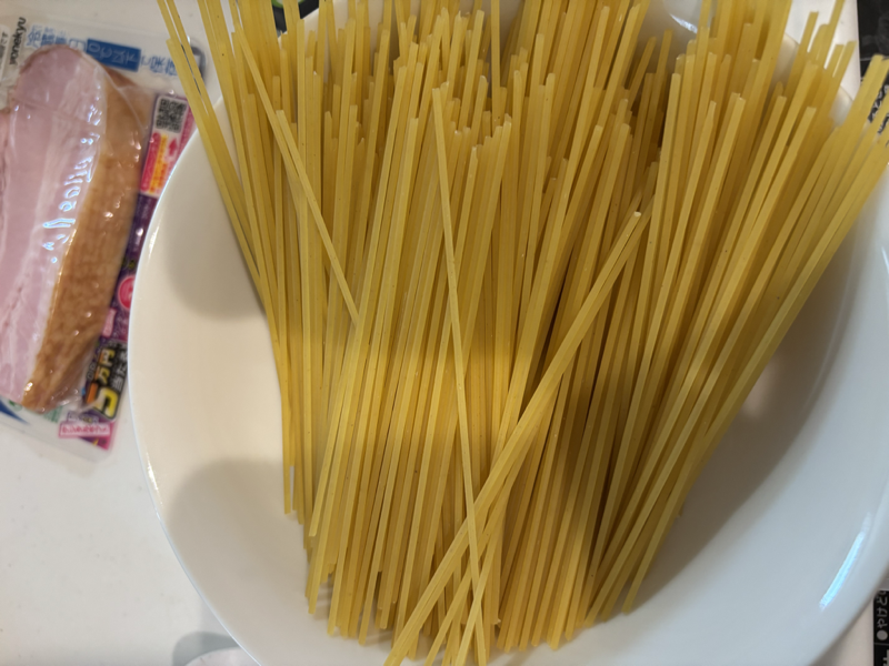 皿に入れたスパゲッティとパック入りのブロックベーコン
